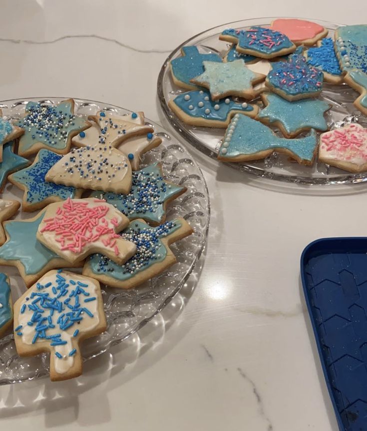 two plates filled with decorated cookies sitting on top of a white counter next to an ice tray