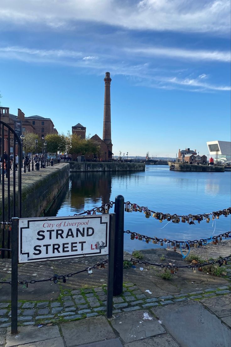 there is a sign that says strand street in front of the water and buildings on the other side