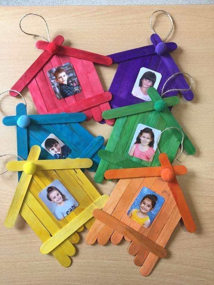 four popsicle house ornaments with pictures hanging from the front and sides, each decorated in different colors