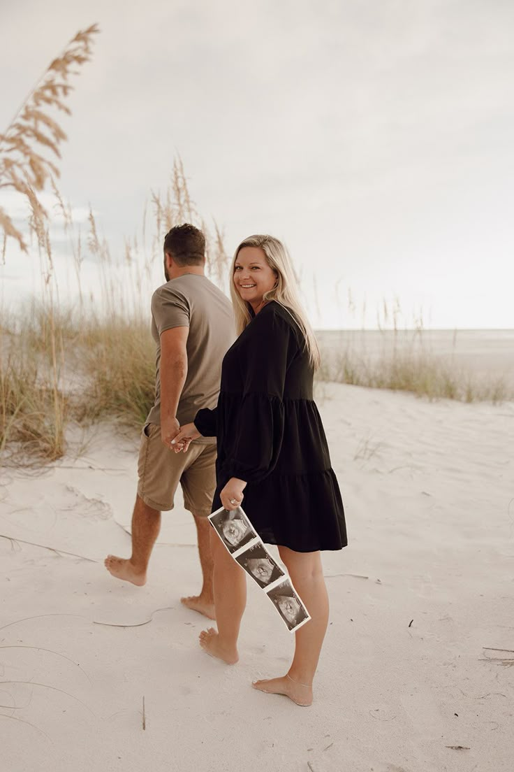 a man and woman are walking on the beach with an old photo in their hand