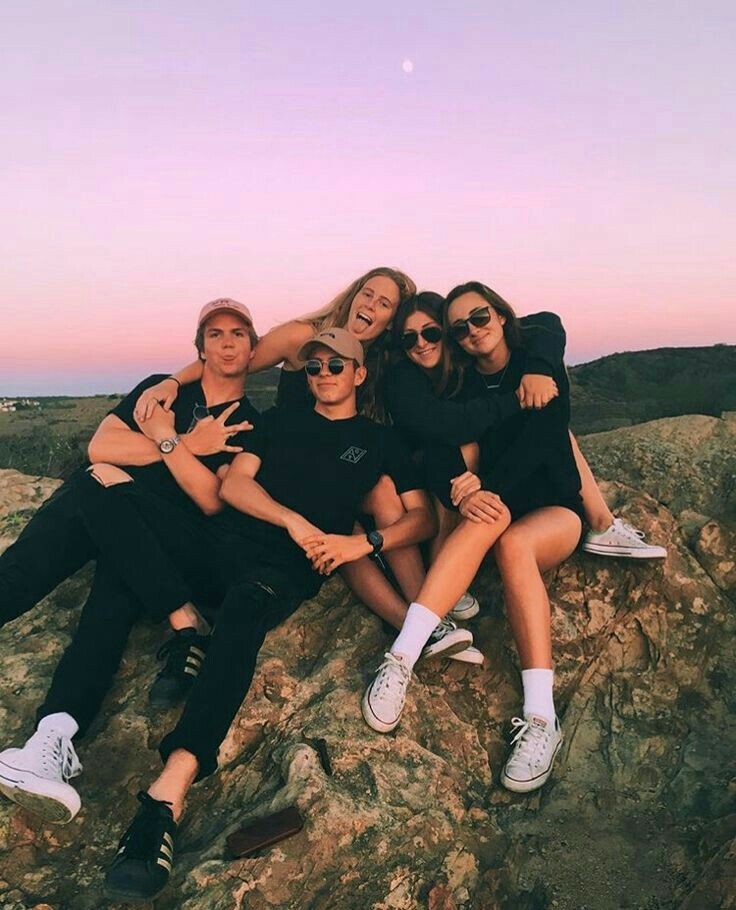 a group of people sitting on top of a large rock next to each other with their arms around one another