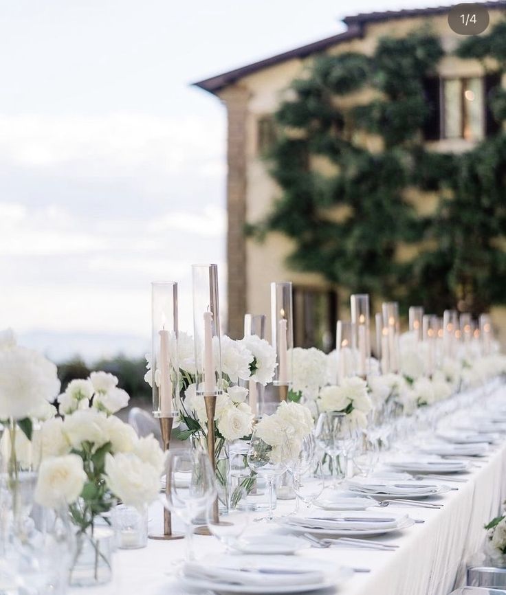 a long table is set with white flowers and candles for an elegant wedding reception in front of a large building