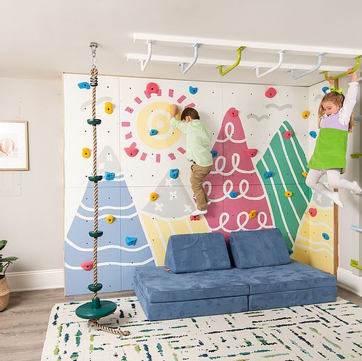 two children climbing up the side of a wall with colorful decorations on it and hanging from hooks