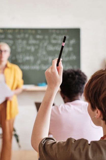 a group of people sitting in front of a blackboard while one person holds up a pen