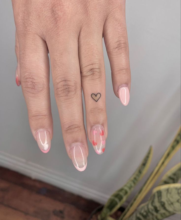 a woman's hand with a heart tattoo on her left ring finger and pink nail polish