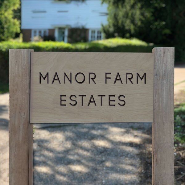 a sign that says manor farm estate in front of a white house with trees and bushes