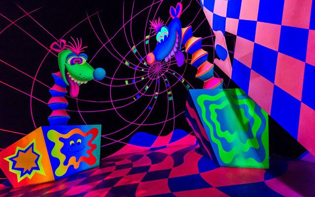 brightly colored artwork on display in a dark room with checkered walls and flooring