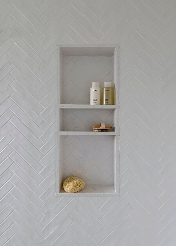 a white shelf with some items on it in a room that is decorated with herringbone tile