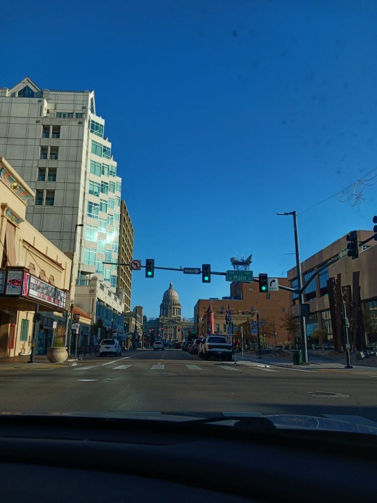 an intersection with traffic lights and buildings in the background on a sunny day, as seen from inside a car