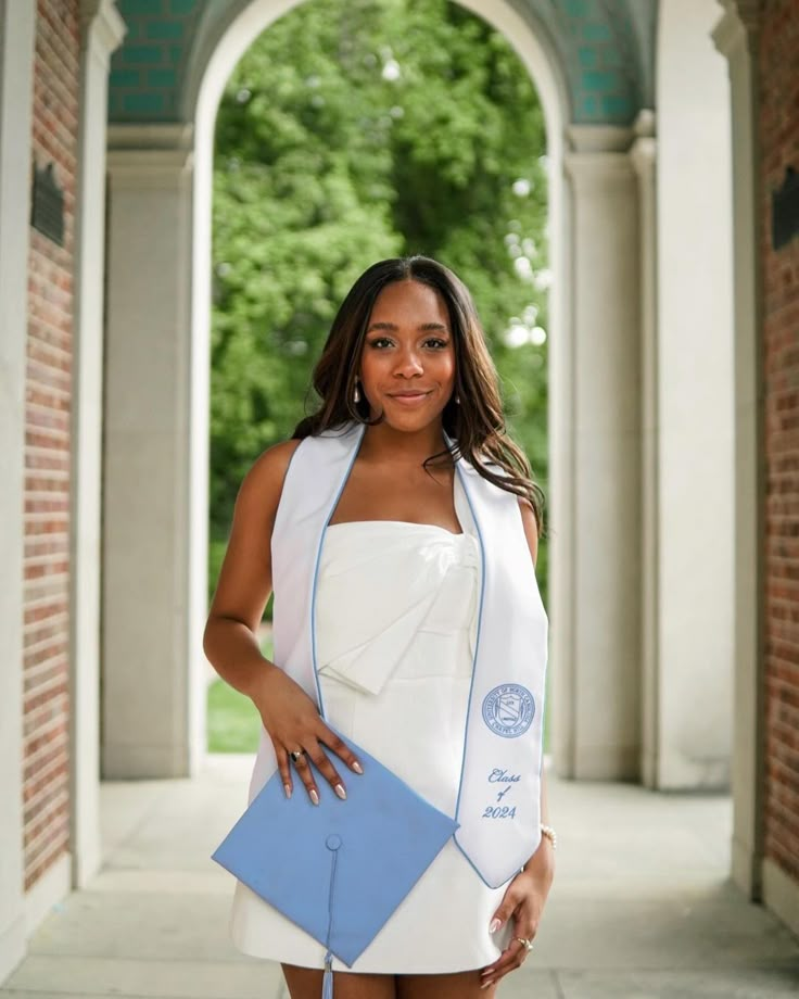 a woman in a white and blue graduation gown posing for the camera with her hand on her hip