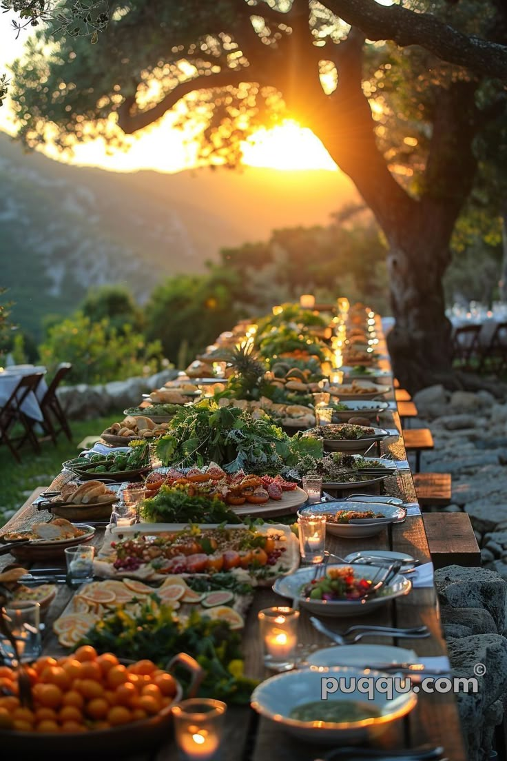 a long table filled with lots of food on top of a grass covered field next to a tree