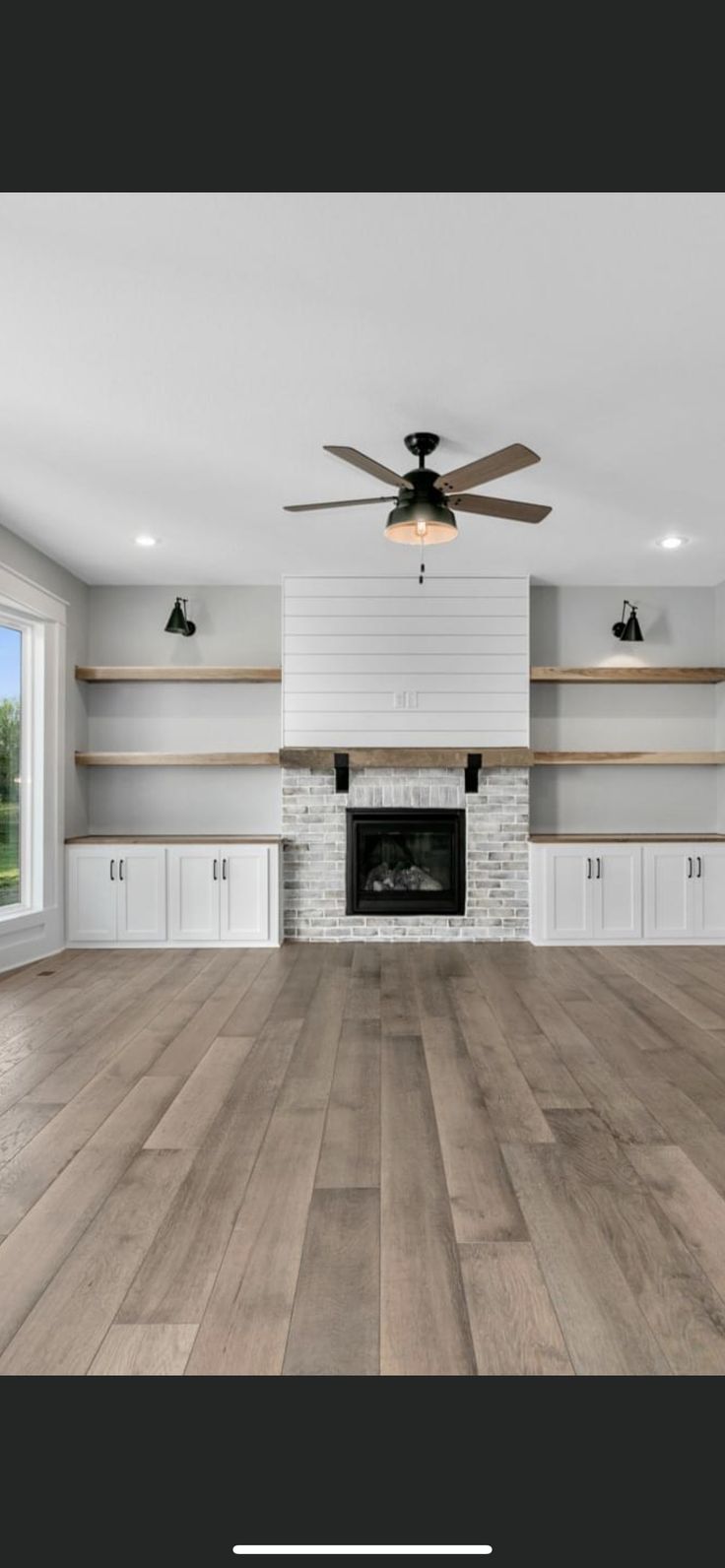 an empty living room with wood flooring and ceiling fan in the middle of it