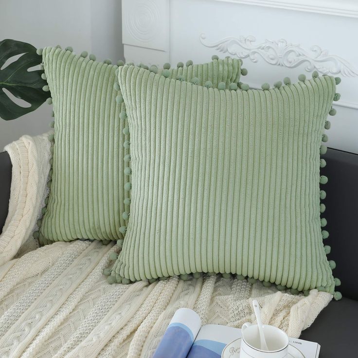 two green pillows sitting on top of a couch next to a cup and saucer