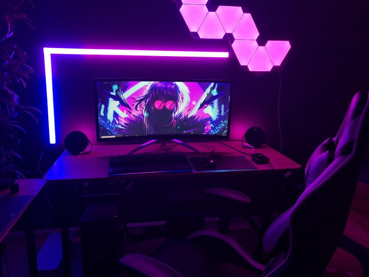 a desktop computer sitting on top of a wooden desk in front of a neon light