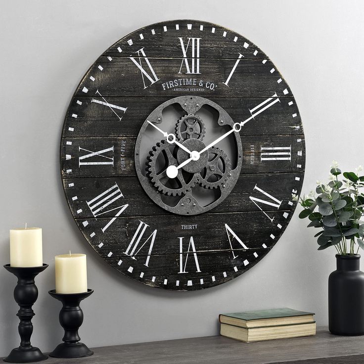 a wooden clock with roman numerals on the face next to candles and flowers