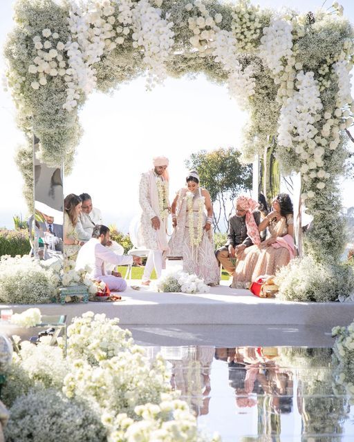 a group of people that are standing in front of a flower covered arch with white flowers on it