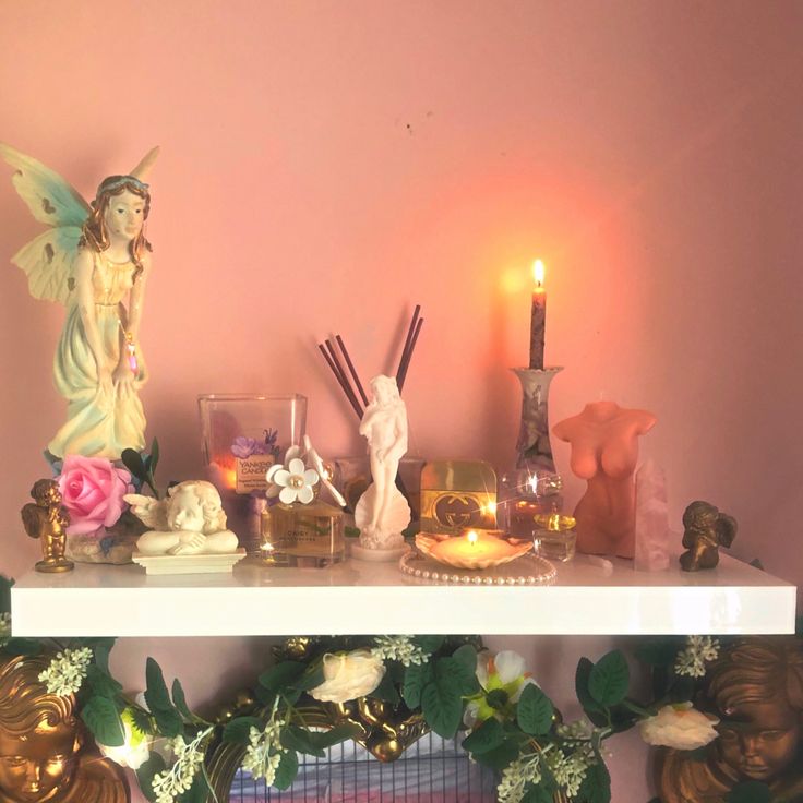 candles, figurines and other decorations are on a mantle in front of a pink wall