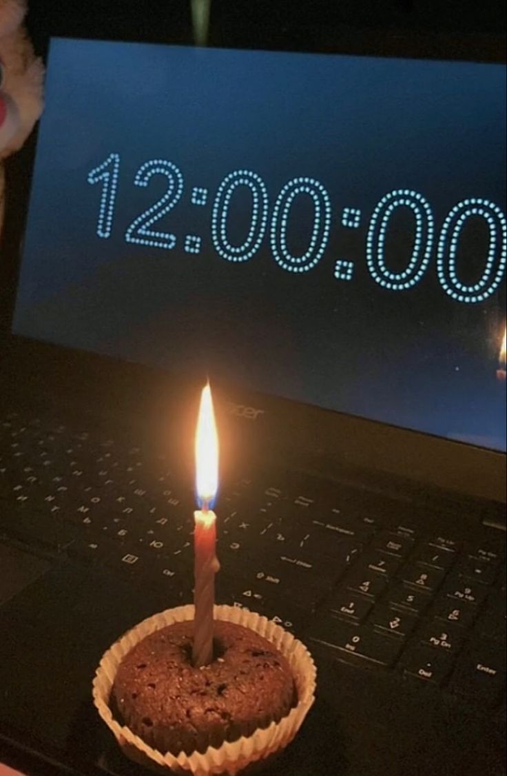 a cupcake with a lit candle sitting in front of a laptop computer that reads 12, 000