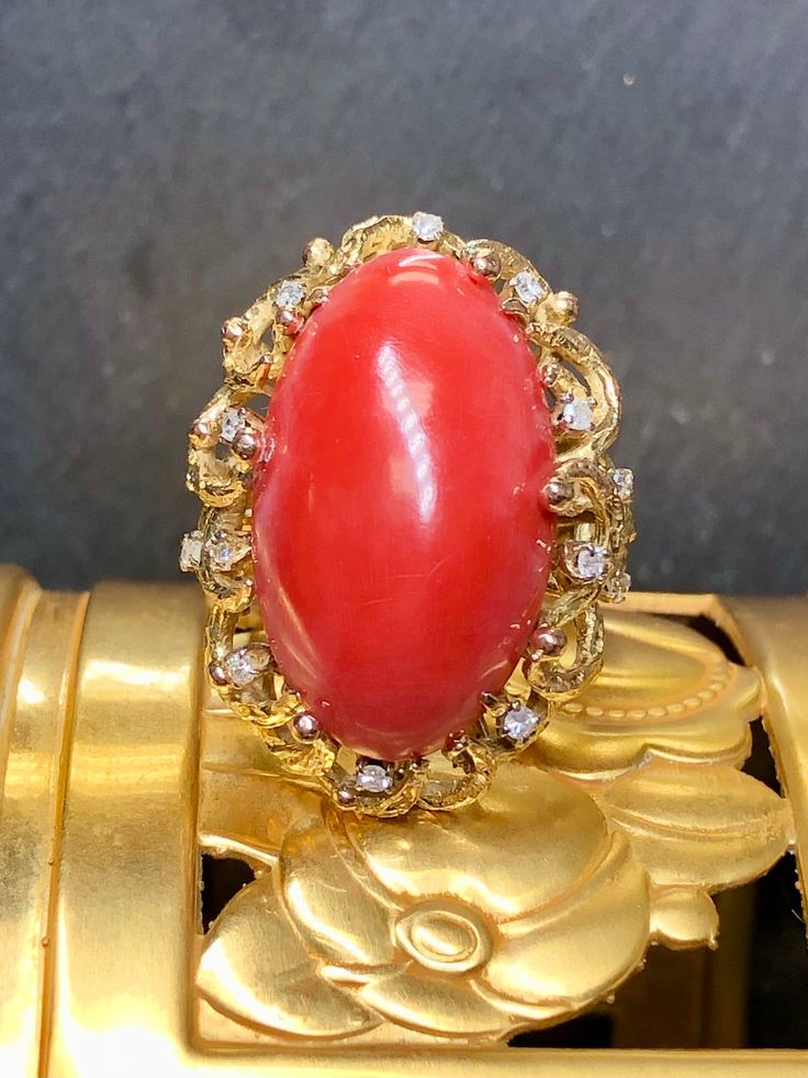 A bold, vintage cocktail ring c. the 1960's crafted in 14K yellow gold and centered by a large cabochon cut natural coral (23.76mm x 14.25mm x 7.40mm) . The color is even and deep... and of course natural. Surrounding the coral are prongs set round diamonds being H-J in color and Si1-i2 in clarity. Dimensions/Weight: Ring measures 1.25" by .75" and weighs 13.4g. Size 6.5 (sizable). Condition: All stones are secure and ring is freshly polished. R-SKKL Gold Round Red Coral Jewelry, Vintage Red Coral Round Bead Jewelry, Luxury Coral Gemstone Ring, Vintage Orange Cabochon Rings, Coral Oval Cabochon Jewelry, Vintage Cocktail Ring, Natural Coral, Diamond Cocktail Rings, Red Coral