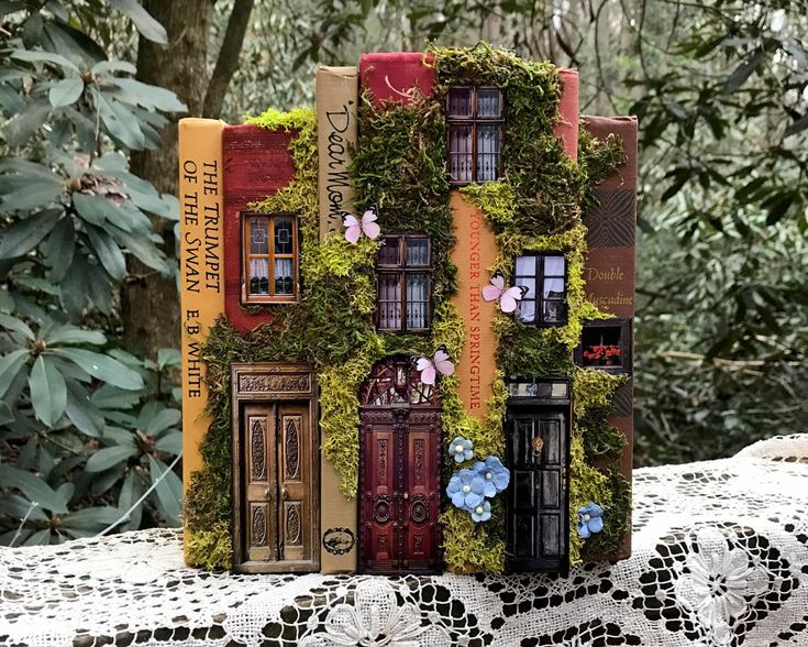 there is a miniature house made out of books with flowers on the front and sides