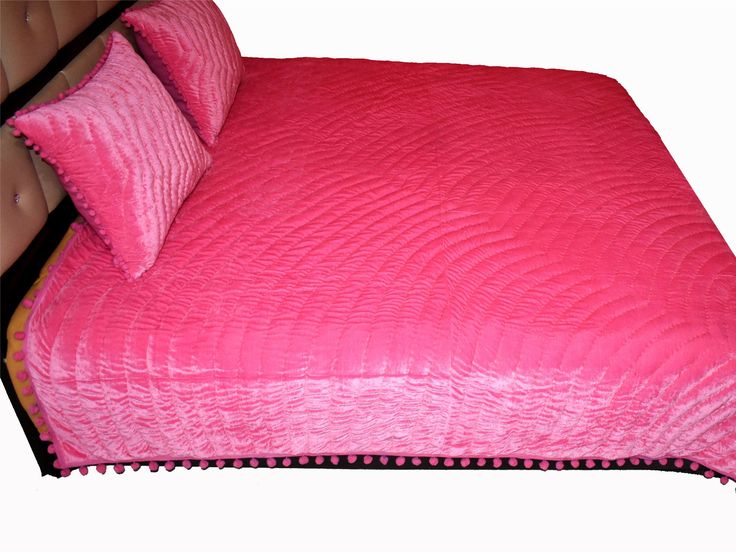 a bed with pink bedspread and two pillows on top of the headboard