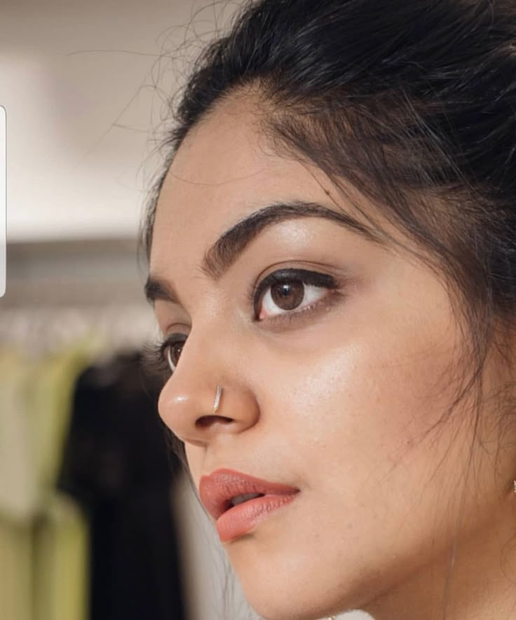 a close up of a person wearing earring next to a hanger with clothes on it