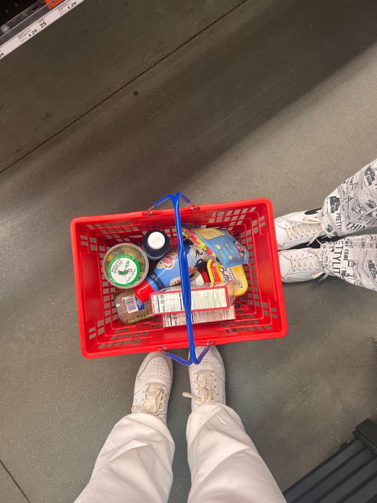 a person holding a red shopping basket filled with items