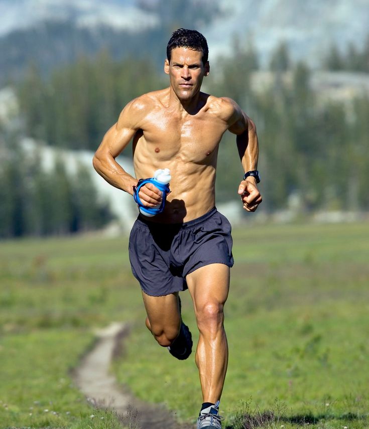 a shirtless man running in the grass with a water bottle on his left hand