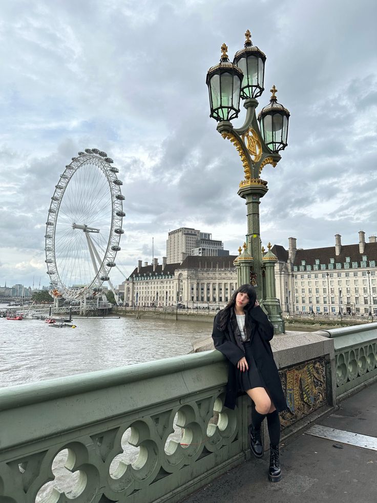 a woman leaning against a lamp post on the side of a bridge next to a body of water