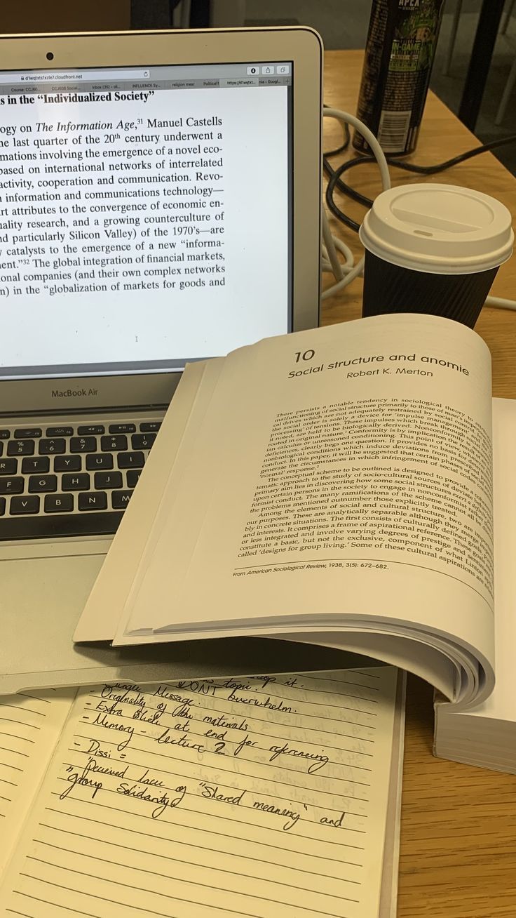 an open book sitting on top of a desk next to a laptop computer and coffee cup