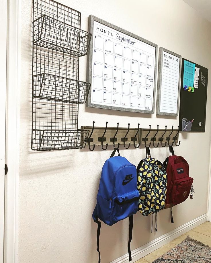 several backpacks are hanging on the wall in front of a calendar and bulletin board