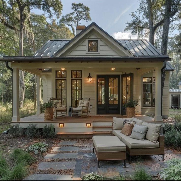 a porch with chairs and couches in front of a house surrounded by trees, shrubs and grass