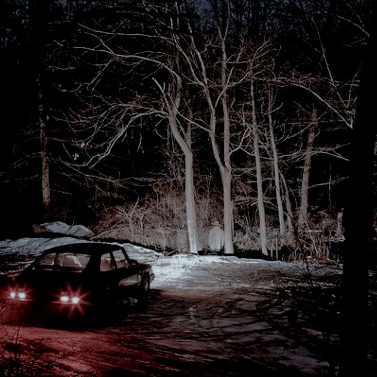 a car is parked in the snow at night with its headlights turned on and trees behind it