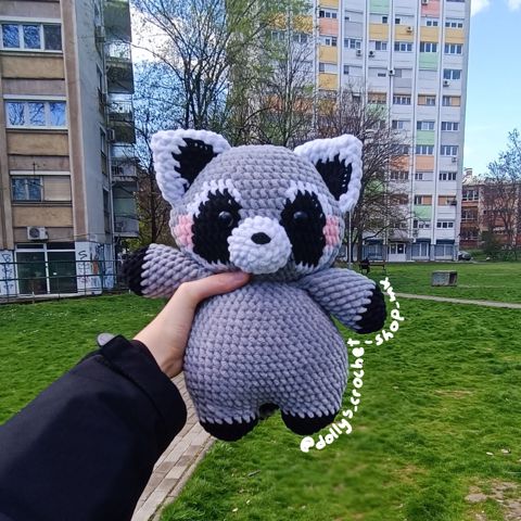 a person holding up a stuffed animal in the grass with buildings in the back ground