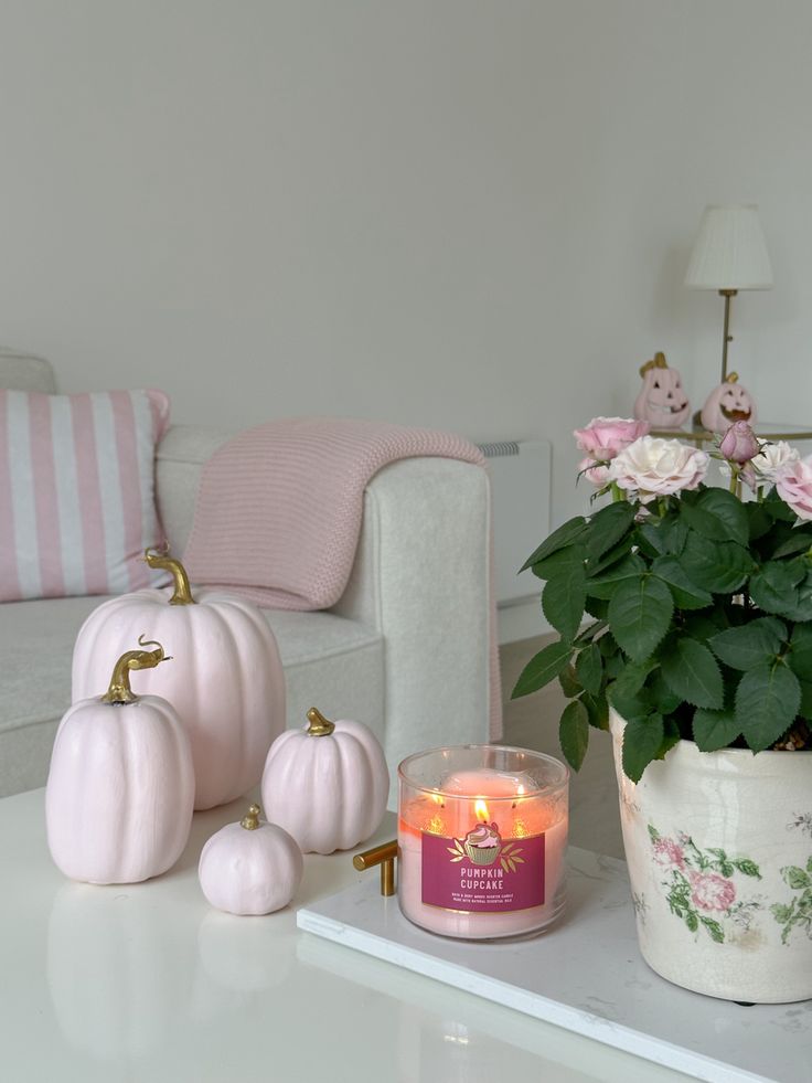 a white table topped with a potted plant next to a candle and some pink flowers