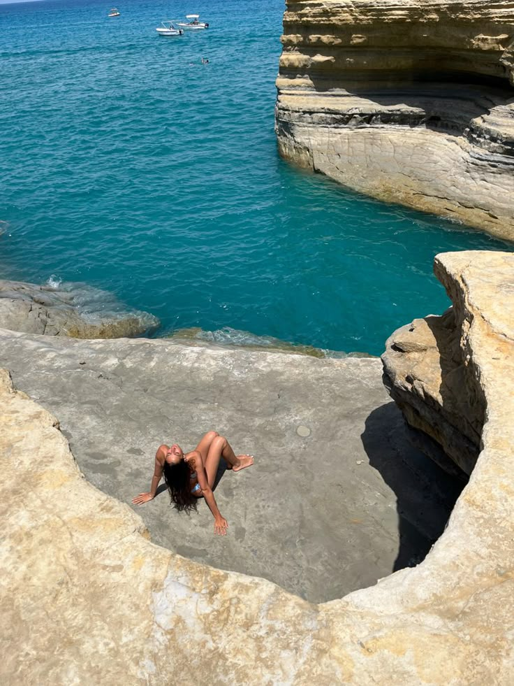 a woman laying on top of a cliff next to the ocean