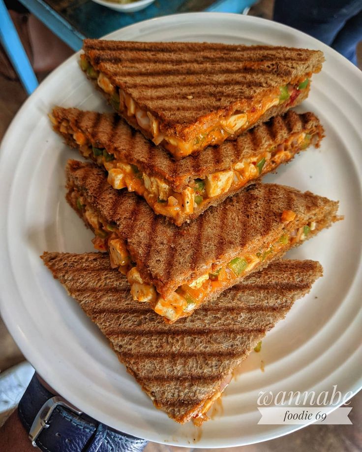 three grilled sandwiches stacked on top of each other on a white plate with a bowl of soup in the background