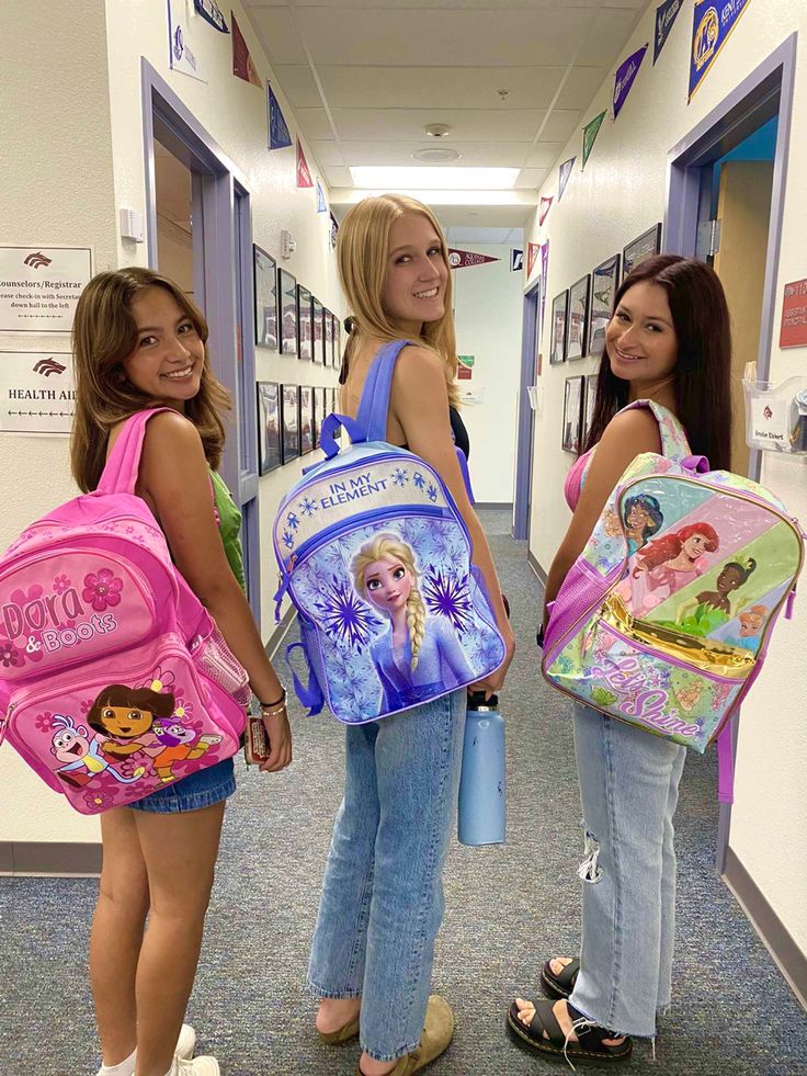 three girls with backpacks are standing in a hallway