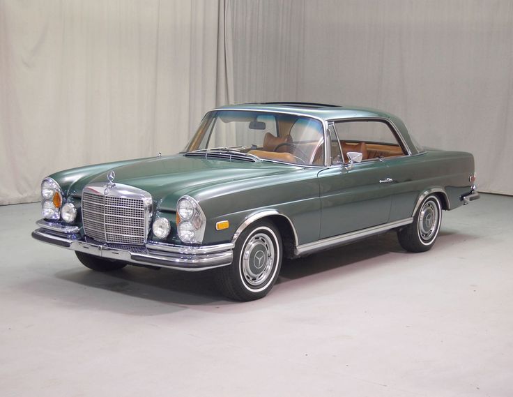 an old green car parked in front of a white curtained wall with the door open