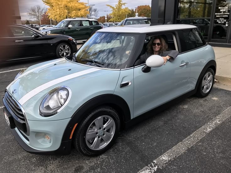 a woman driving a light blue mini cooper in a parking lot