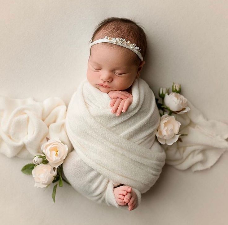 a newborn baby wrapped in a white blanket with flowers around it's sides and her head resting on her hands