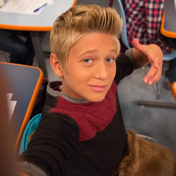 a young boy sitting in a classroom with his hand on his head and looking at the camera