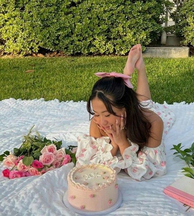 a woman laying on the ground with a cake in front of her and flowers behind her