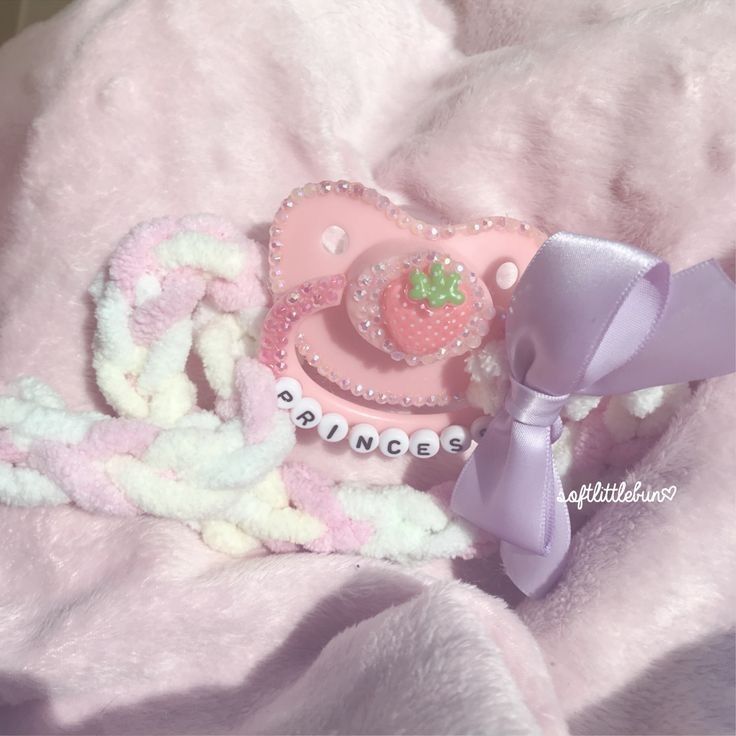 a pink teddy bear laying on top of a blanket with a pacifier and other items