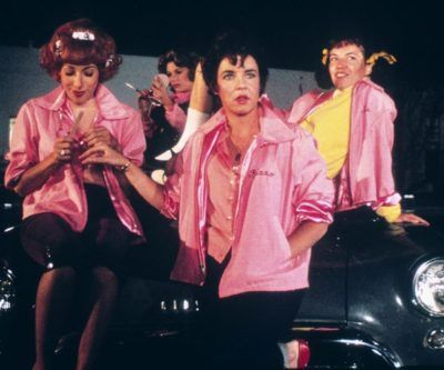 three women in pink shirts and black shorts standing next to each other near a car