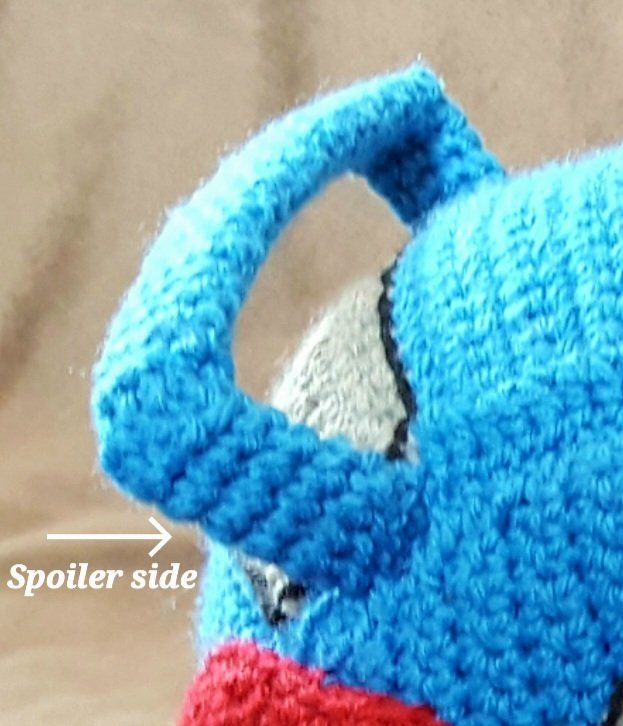 a crocheted blue and red teapot with an arrow pointing to the right