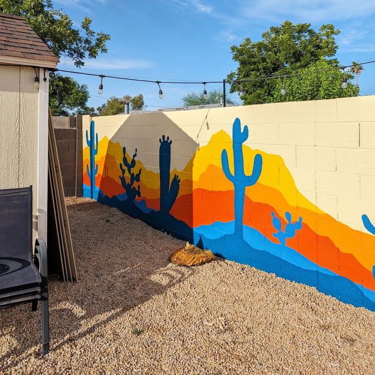 a colorful mural on the side of a building in an area with gravel and trees