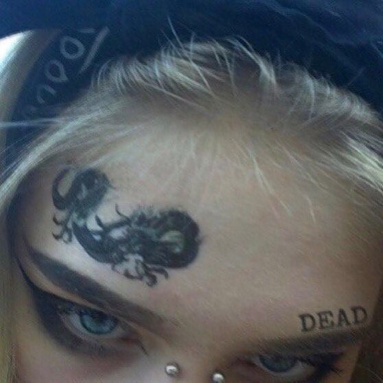 a woman with dragon tattoos on her face and nose is looking at the camera while wearing a black hoodie