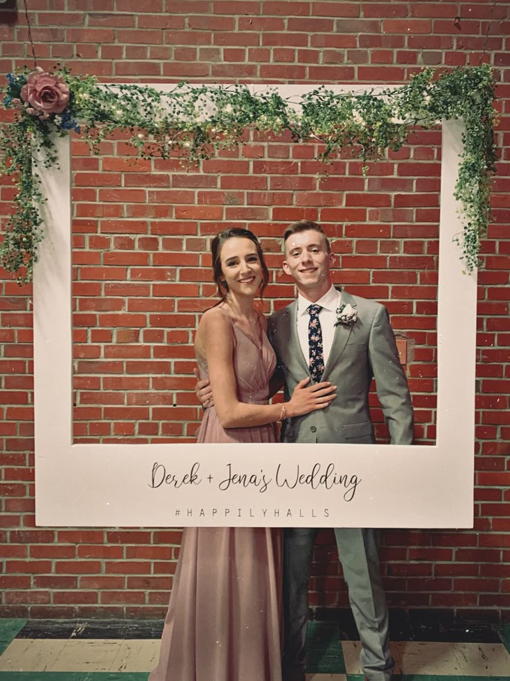 a man and woman standing next to each other in front of a brick wall holding a sign