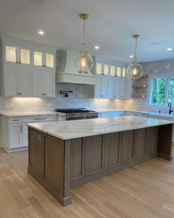 a large kitchen with an island in the middle and two pendant lights hanging from the ceiling